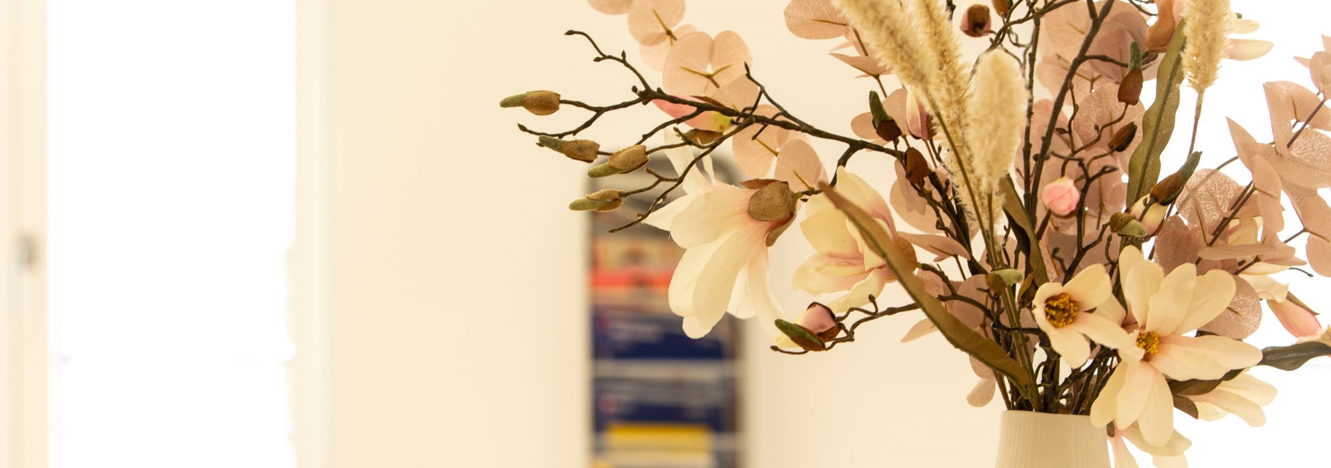 Eine Nahaufnahme einer Vase mit rosa Blumen bestückt. Im Hintergrund sieht man einen Zeitungsständer.