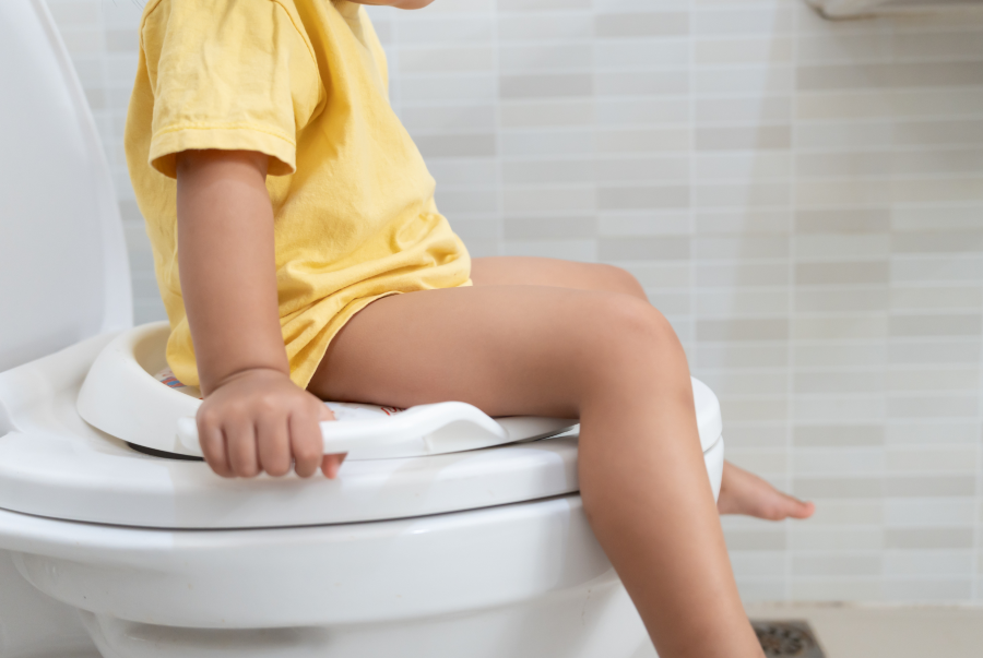 Ein kleiner Bub sitzt auf einem Kindertoiletten-Aufsatz auf einer Toilette und hält sich fest.